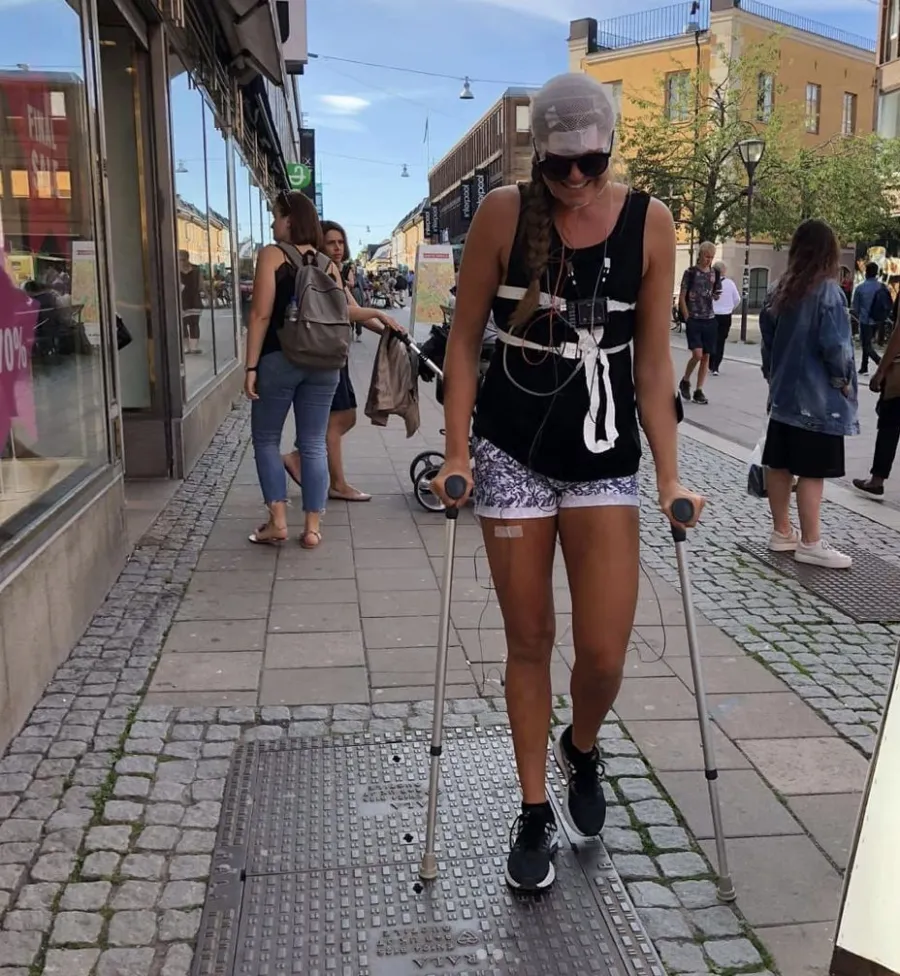 Emma on crutches in a city street, wired up with a pain-monitoring harness after surgery